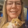Smiling woman wearing glasses holding a ginger and white kitten close to her face.
