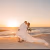 Bride and groom embracing and twirling on a beach at sunset with waves in the background.